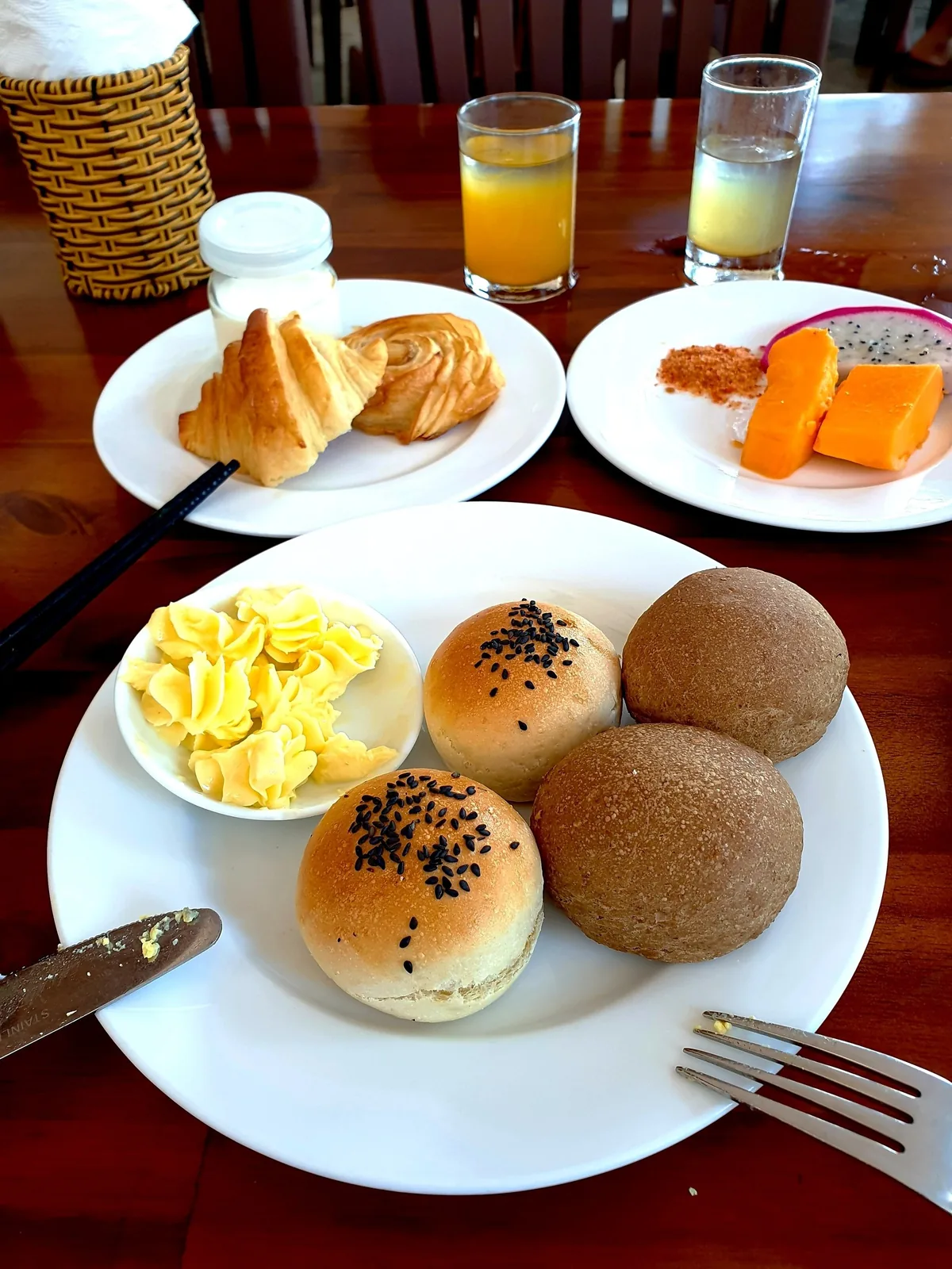 A breakfast table in Mui Ne with bread rolls, butter, pastries, tropical fruit and juice.